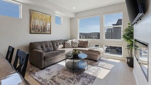 Ein modernes Wohnzimmer mit einem grauen Sofa, einem Couchtisch und einem großen Fenster mit Blick auf die Stadt.
