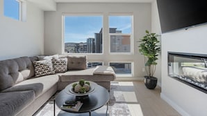 Ein modernes Wohnzimmer mit einem grauen Sofa, einem Couchtisch und einem großen Fenster mit Blick auf die Stadt.