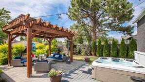 Une pergola en bois avec un espace salon extérieur, un jacuzzi et un jardin bien entretenu.