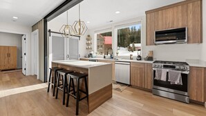 A modern kitchen with a central island, bar stools, a built-in oven, and a large window providing a view of the outdoors. - Summer Getaway | Pool Table, Foosball & Views (Brian Head)
