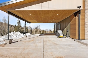 A covered outdoor area with a concrete floor, a covered walkway, and a snow-covered landscape in the background.