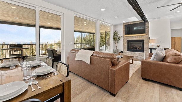 A modern living room with a fireplace, leather sofas, a dining area with a table set for two, and large windows offering a view of the outdoors. - Summer Getaway | Pool Table, Foosball & Views (Brian Head)