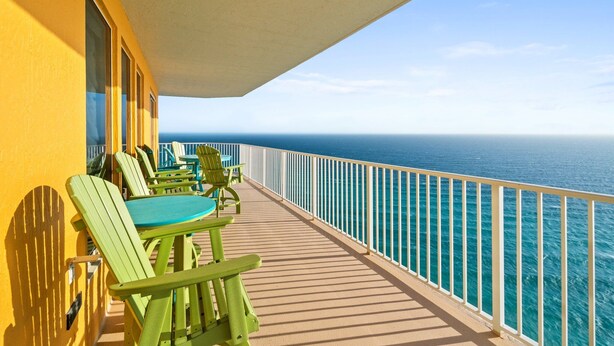 Un balcon avec des chaises vertes et une table, donnant sur une mer bleue et limpide.