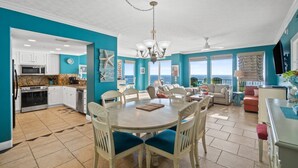 Une cuisine spacieuse avec des meubles blancs, un coin repas avec une table ronde et des chaises, et un salon avec un canapé et des fauteuils.