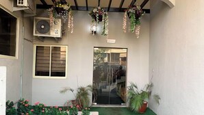 A building entrance with a glass door, a small garden area with plants, and hanging floral decorations. - Harrington Inn  (Ibadan)