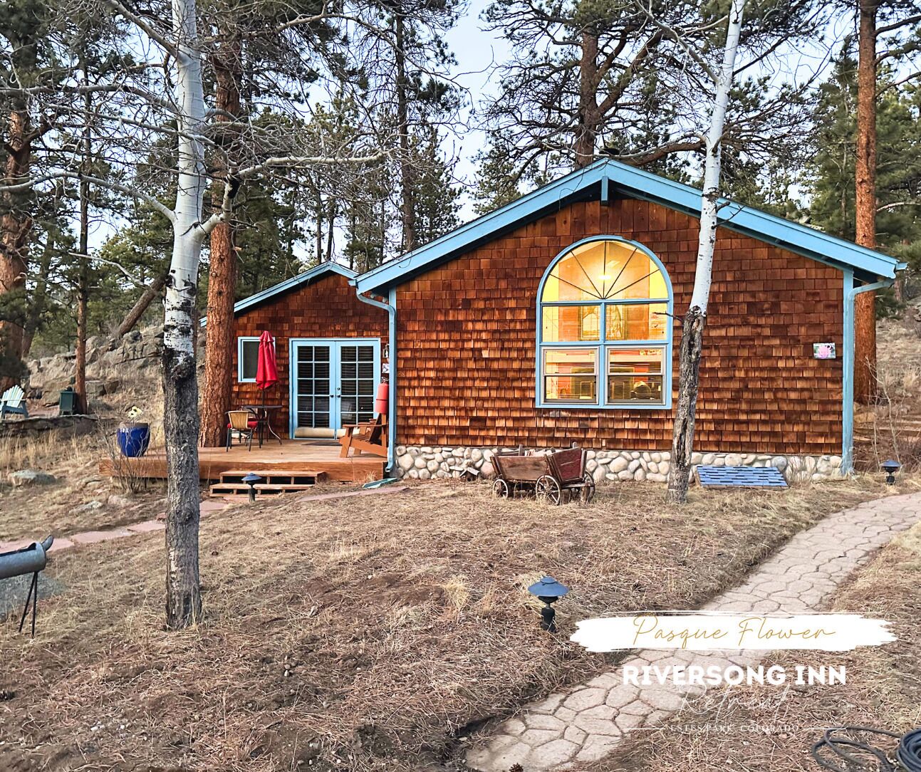 A rustic cabin with a large window, a porch with outdoor seating, and a stone wall foundation.