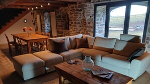 A cozy living room with a sofa, ottoman, wooden coffee table, and a stone wall. - Typical renovated farmhouse - Ideal for a family getaway (Champclause)