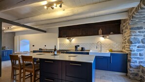 A modern kitchen with a large island, dark cabinetry, and a stone accent wall. - Typical renovated farmhouse - Ideal for a family getaway (Champclause)