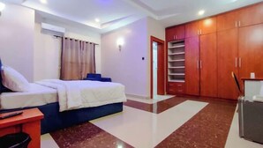 A bedroom with a bed, a desk, a wardrobe, and a bathroom. - E- Exclusive Hotel  (Ibadan)