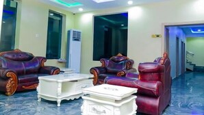 A spacious room with a modern ceiling design, a large air conditioning unit, and a seating area with leather chairs and a white coffee table. - E- Exclusive Hotel  (Ibadan)