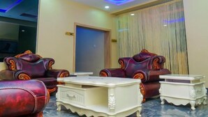 A room with two leather armchairs, a white side table, and a door with a curtain. - E- Exclusive Hotel  (Ibadan)