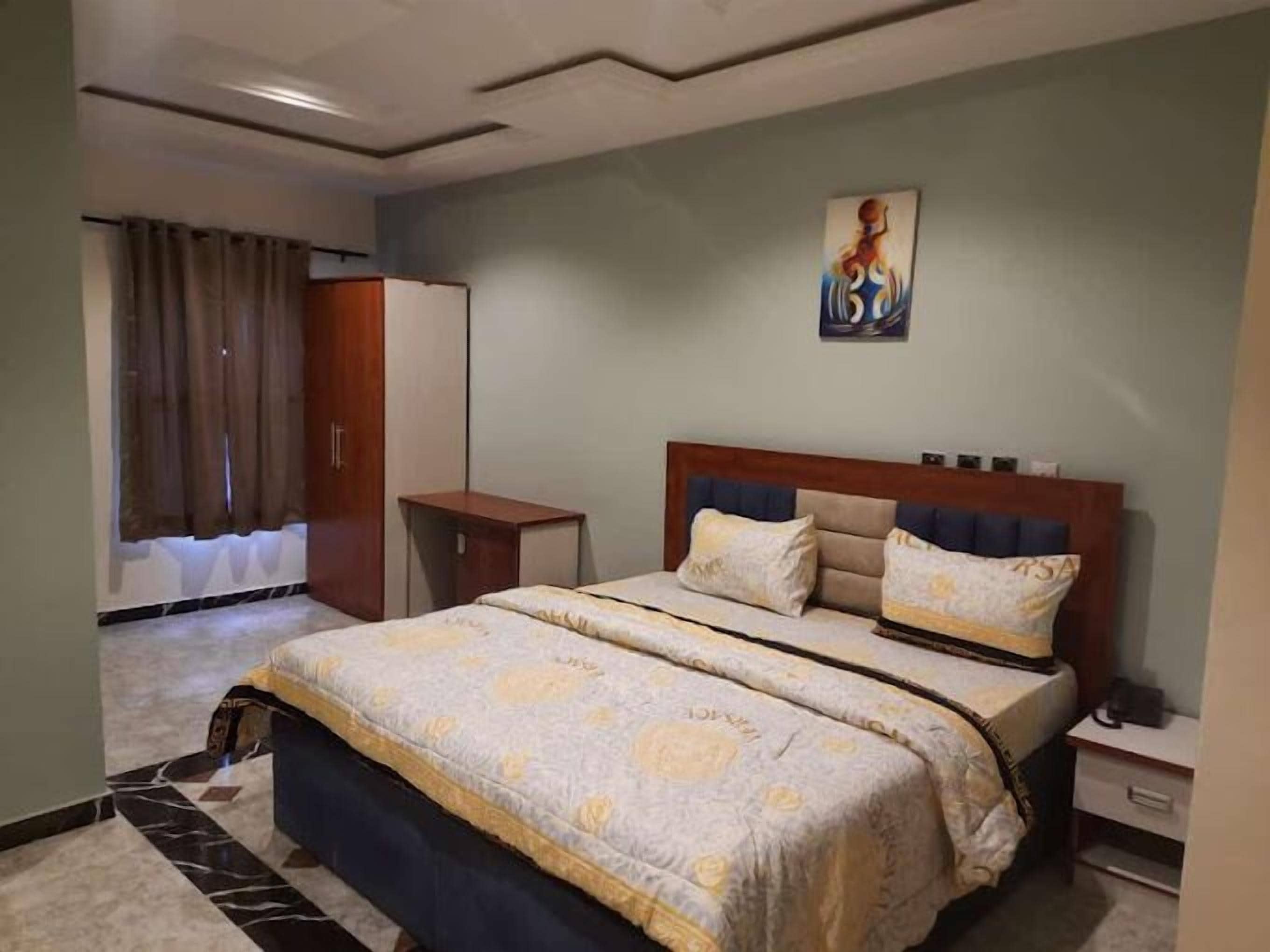 Een hotelkamer met een bed, een nachtkastje, een kledingkast en een schilderij aan de muur.