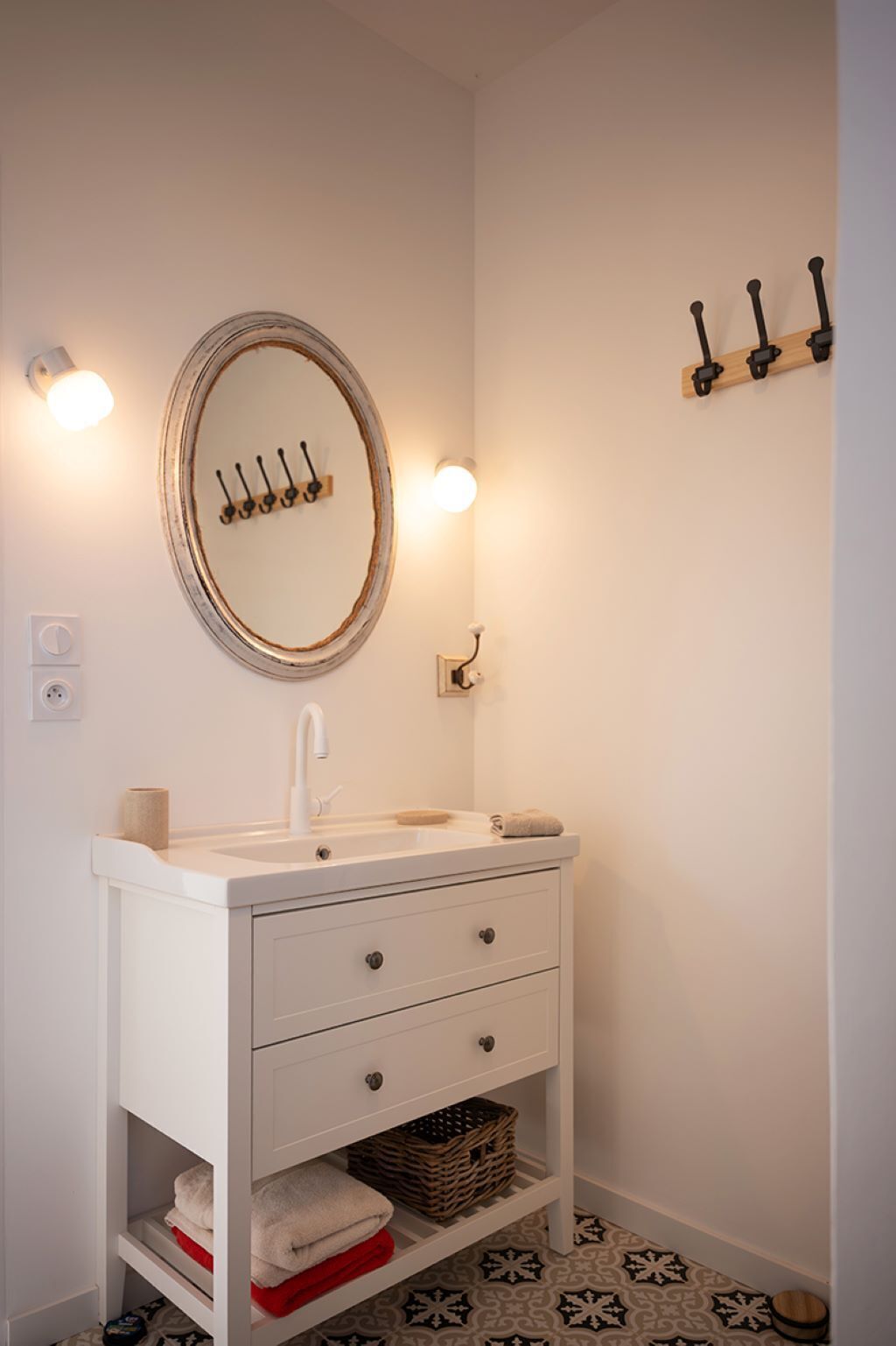 Een badkamer met een wit wastafelmeubel, een ronde spiegel, een handdoekhouder en een vloer met een patroon.