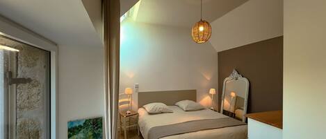 Une chambre à coucher avec un lit, des lampes de chevet, un luminaire suspendu, un tableau et un miroir au mur.