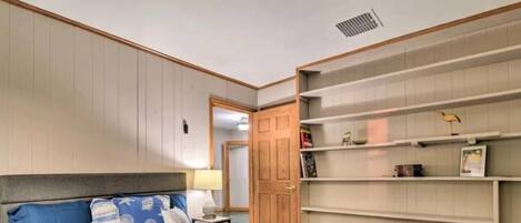 Un dormitorio con una cama, una mesita de noche, una puerta de madera y estanterías empotradas con diversos objetos.