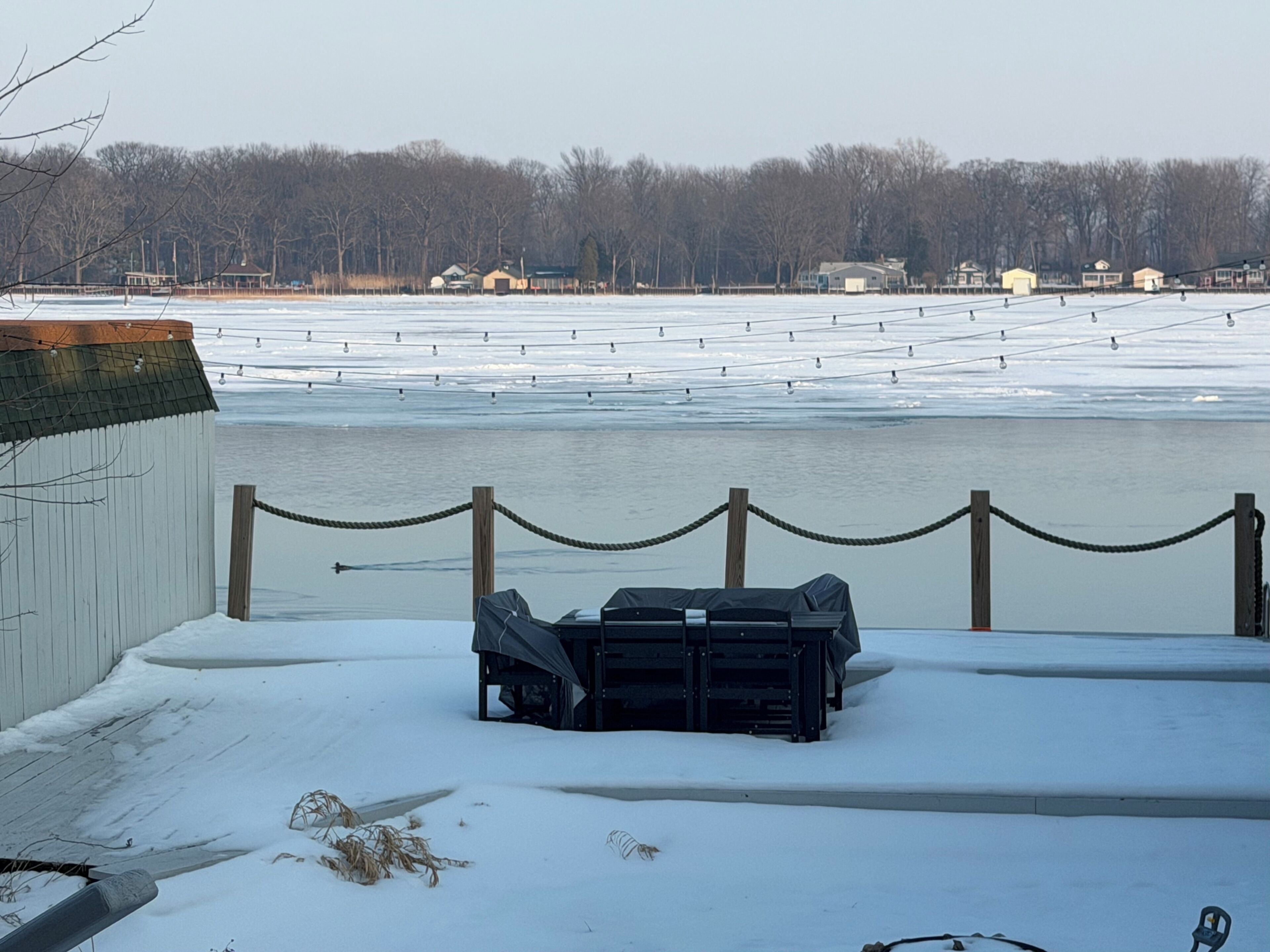 A snow-covered outdoor area with a fenced seating area and a view of a body of water.