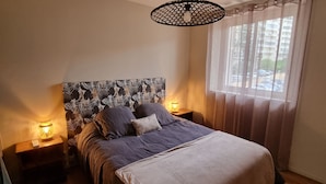 Ein Schlafzimmer mit einem großen Bett, zwei Nachttischen mit Lampen, einem gemusterten Kopfteil und einem Fenster mit Vorhängen.