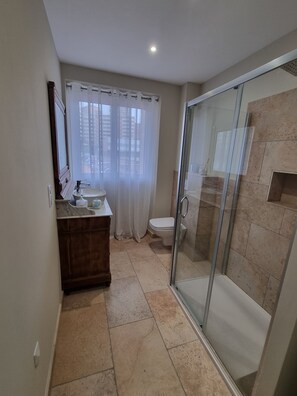 Une salle de bain avec une douche à parois de verre, des toilettes, un meuble-lavabo avec un miroir et une fenêtre avec des rideaux.