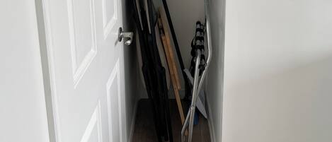 Un pasillo estrecho con una puerta blanca, un perchero con perchas de madera y una silla plegable de metal.