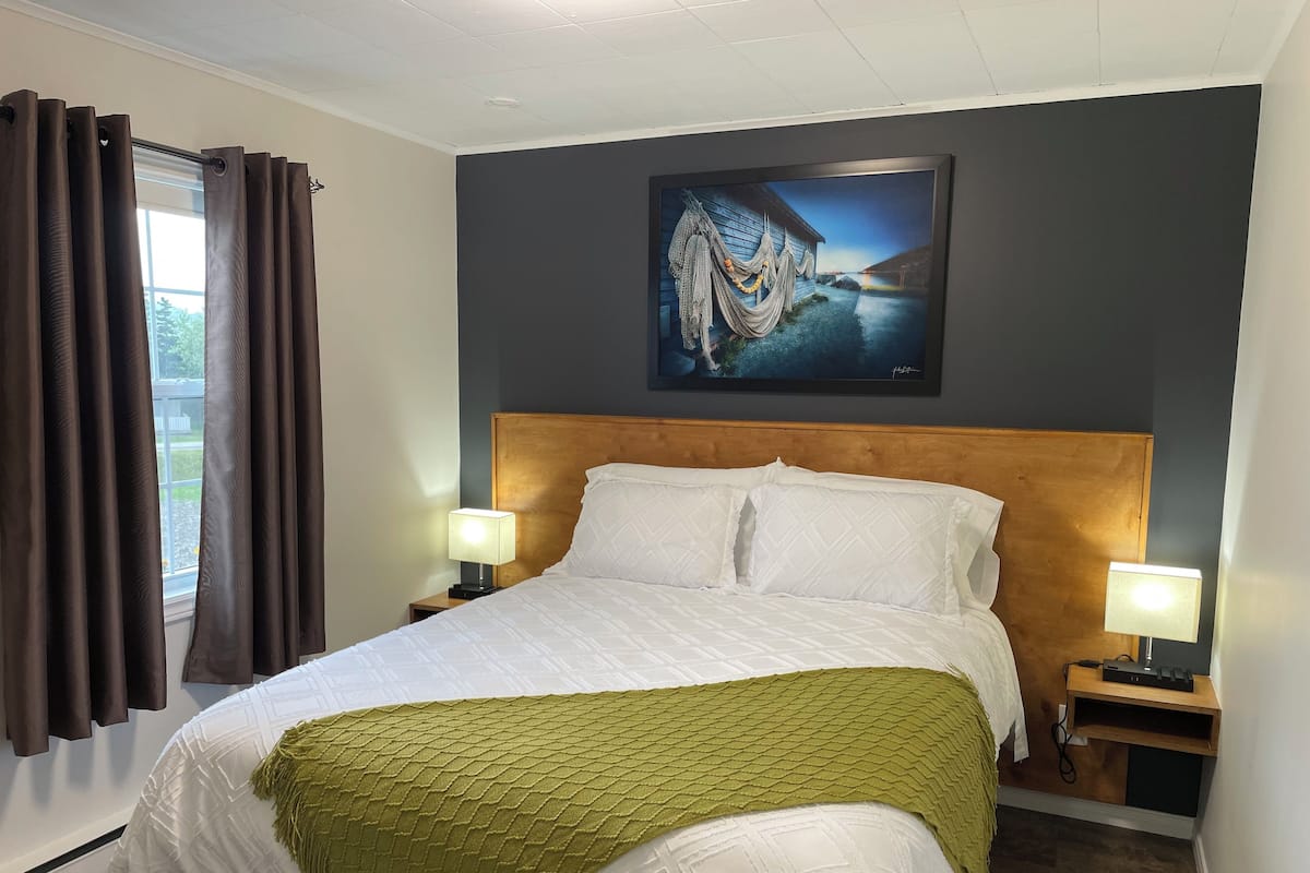 Una habitación de hotel con una cama, dos lámparas de noche, un cuadro en la pared y una ventana con cortinas.
