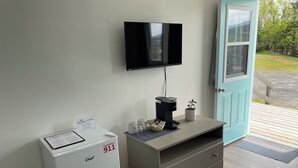A hotel room with a white Chef refrigerator, a coffee maker, a small potted plant, and a flat-screen TV mounted on the wall. - Buoy & Arrow Restaurant and Suites (Rocky Harbour)
