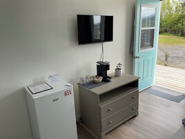 Habitación de hotel con refrigerador blanco marca Chef, cafetera, una pequeña planta en maceta y televisor de pantalla plana montado en la pared.