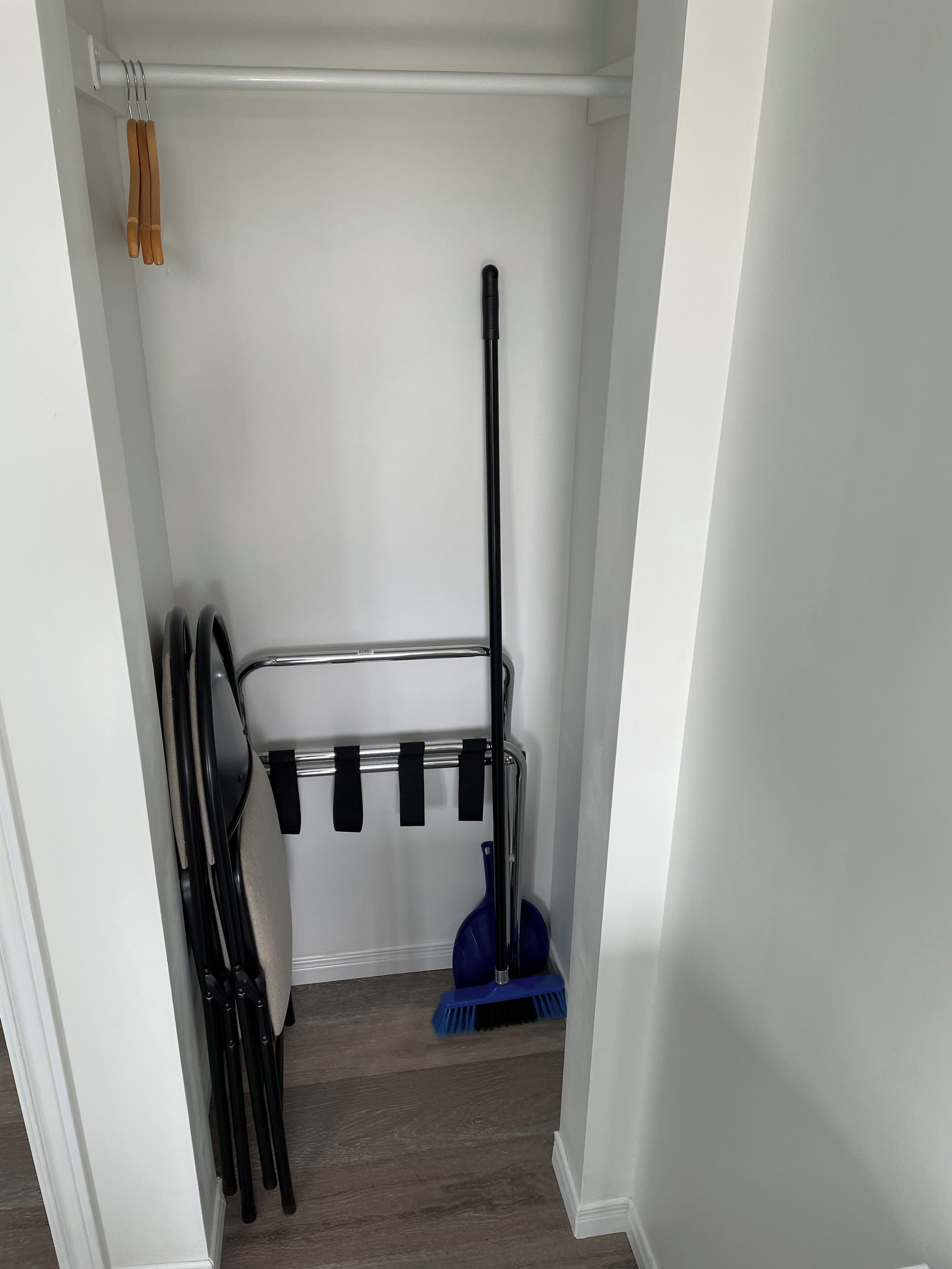 A closet with a metal rack holding black belts and a blue broom.