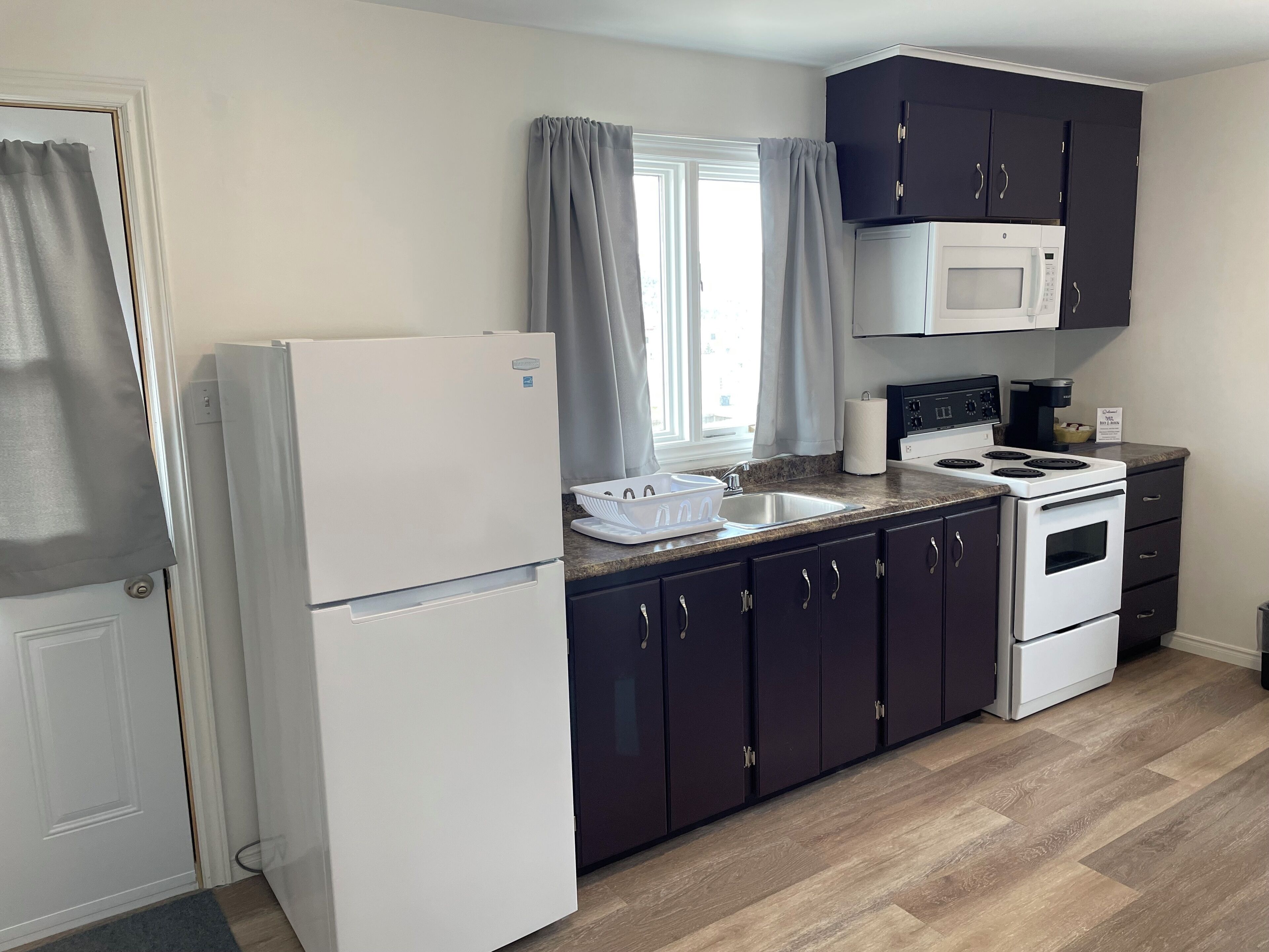 A compact kitchen with a refrigerator, stove, microwave, and dark cabinets.
