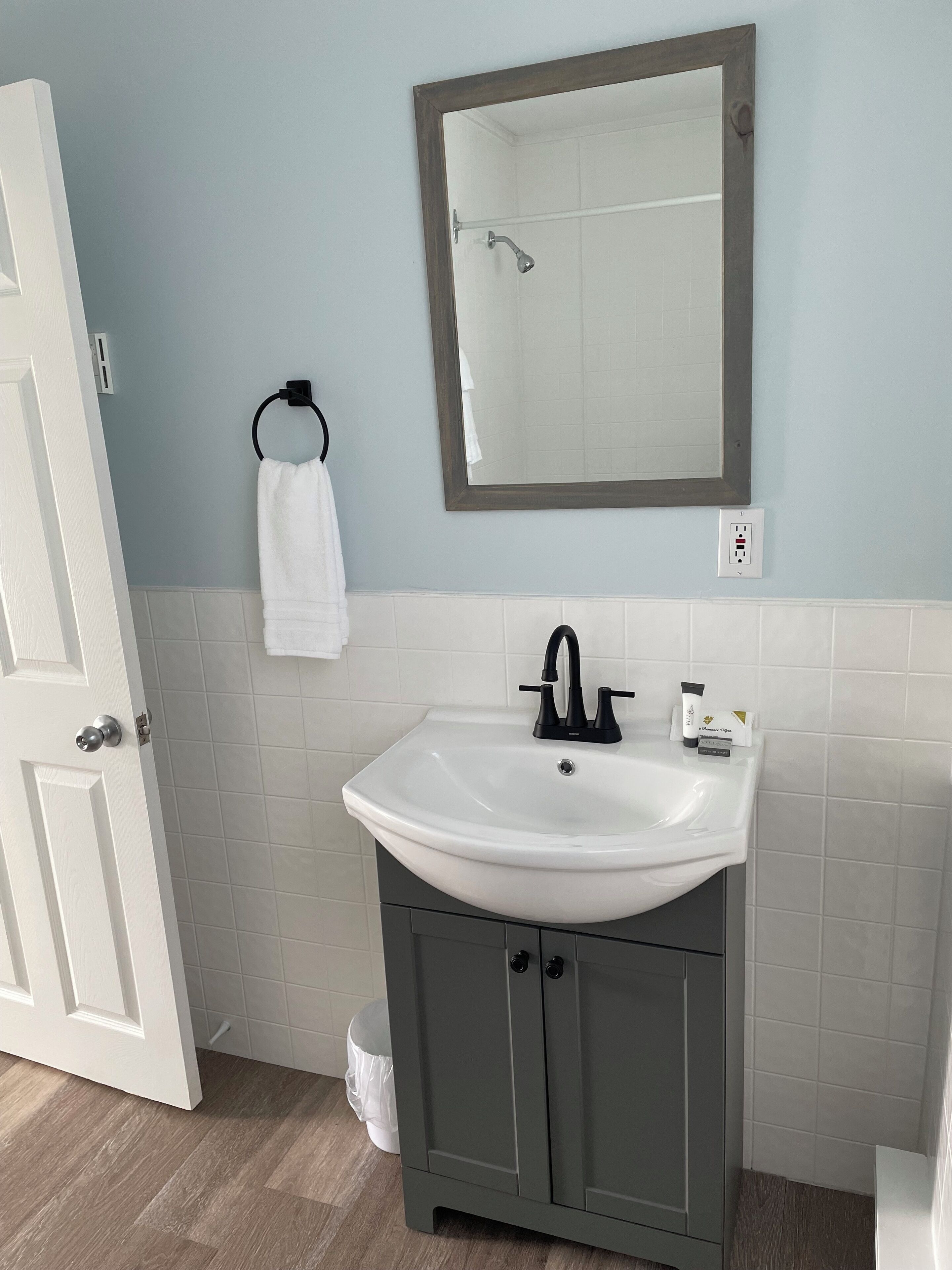Een badkamer met een witte wastafel, donkere kastjes, een handdoekhouder en een spiegel.
