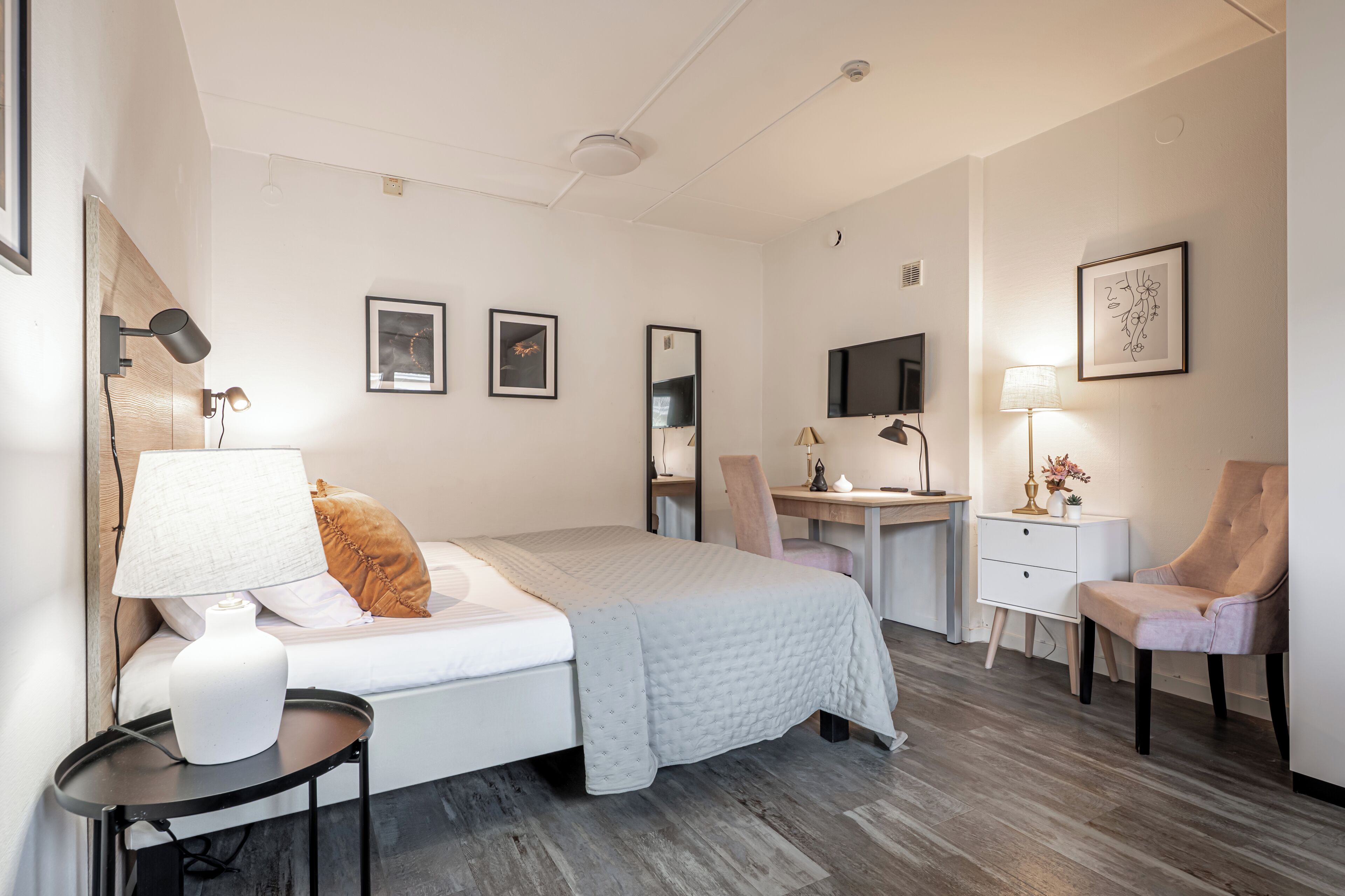 A bedroom with a bed, bedside table, desk, chair, and a TV.