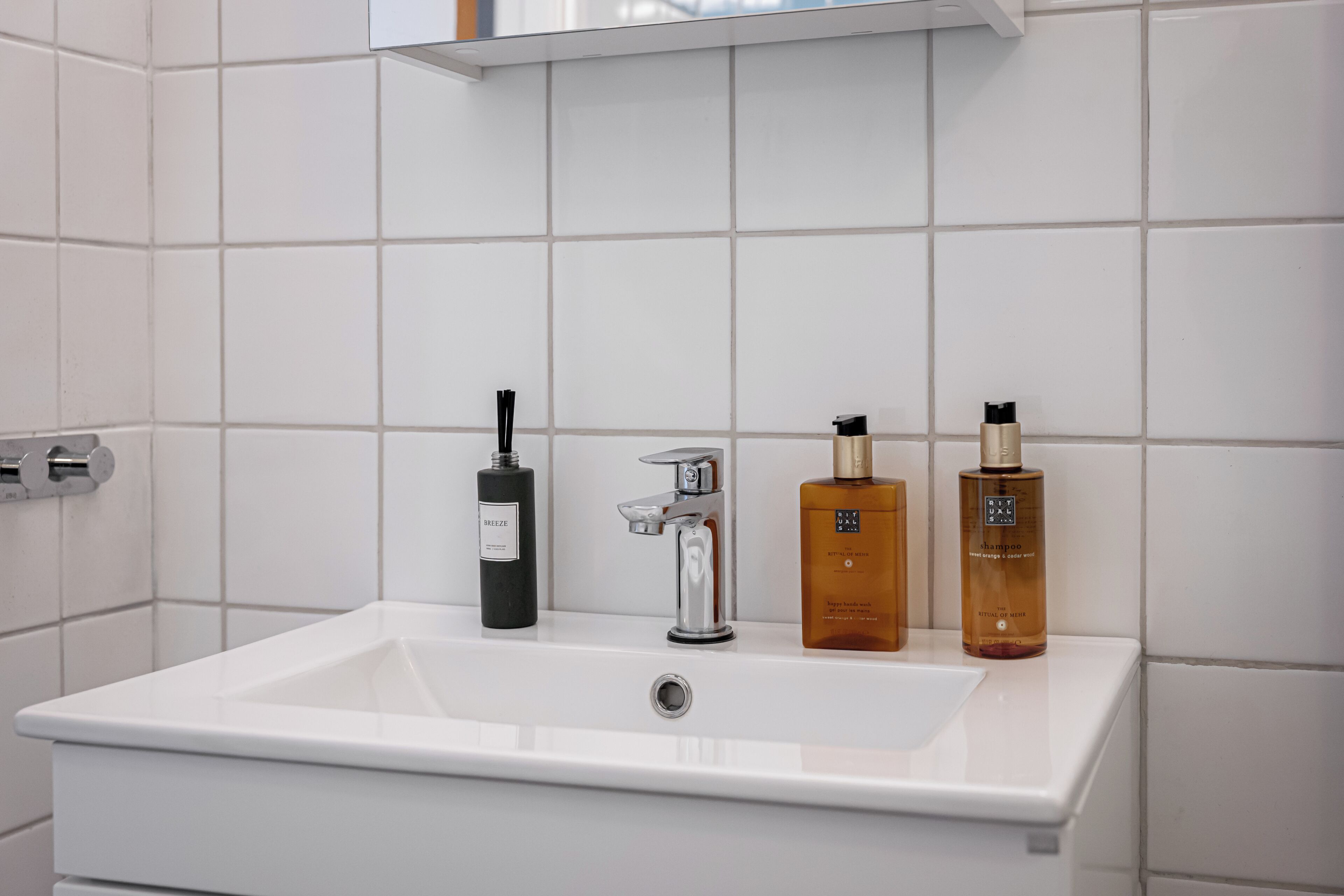 Un baño con un lavamanos blanco, un grifo cromado y tres botellas de jabón líquido.