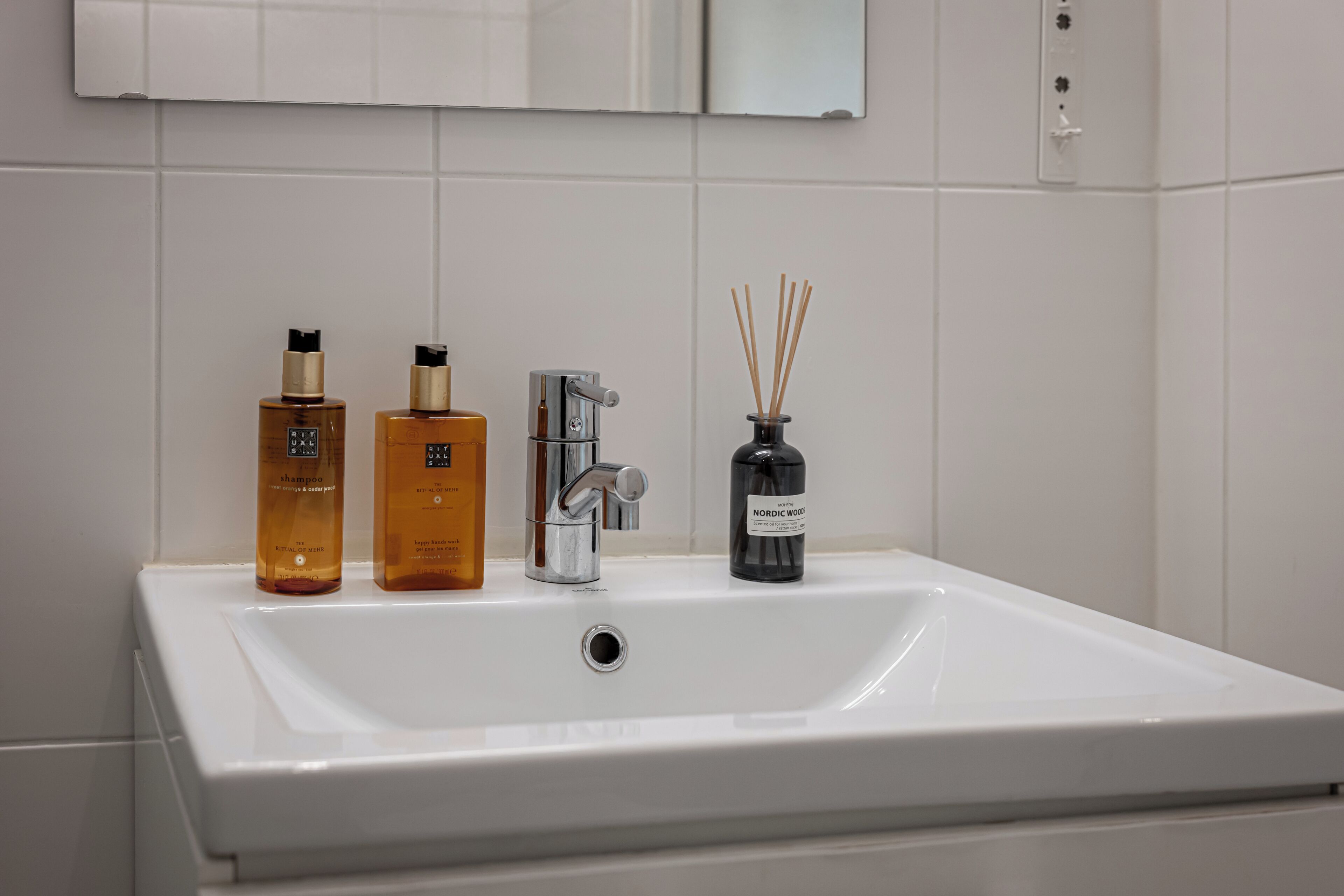 A white bathroom sink with two amber-colored bottles and a black bottle with reed sticks.