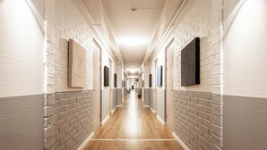Un long couloir étroit aux murs de briques blanches et au plancher en bois, qui mène à plusieurs portes.