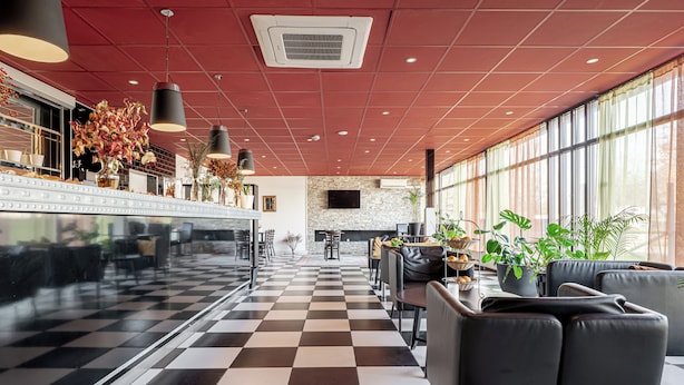 Un hall d’hôtel moderne avec un sol à carreaux, des sièges en cuir, des plantes en pot et une grande fenêtre.