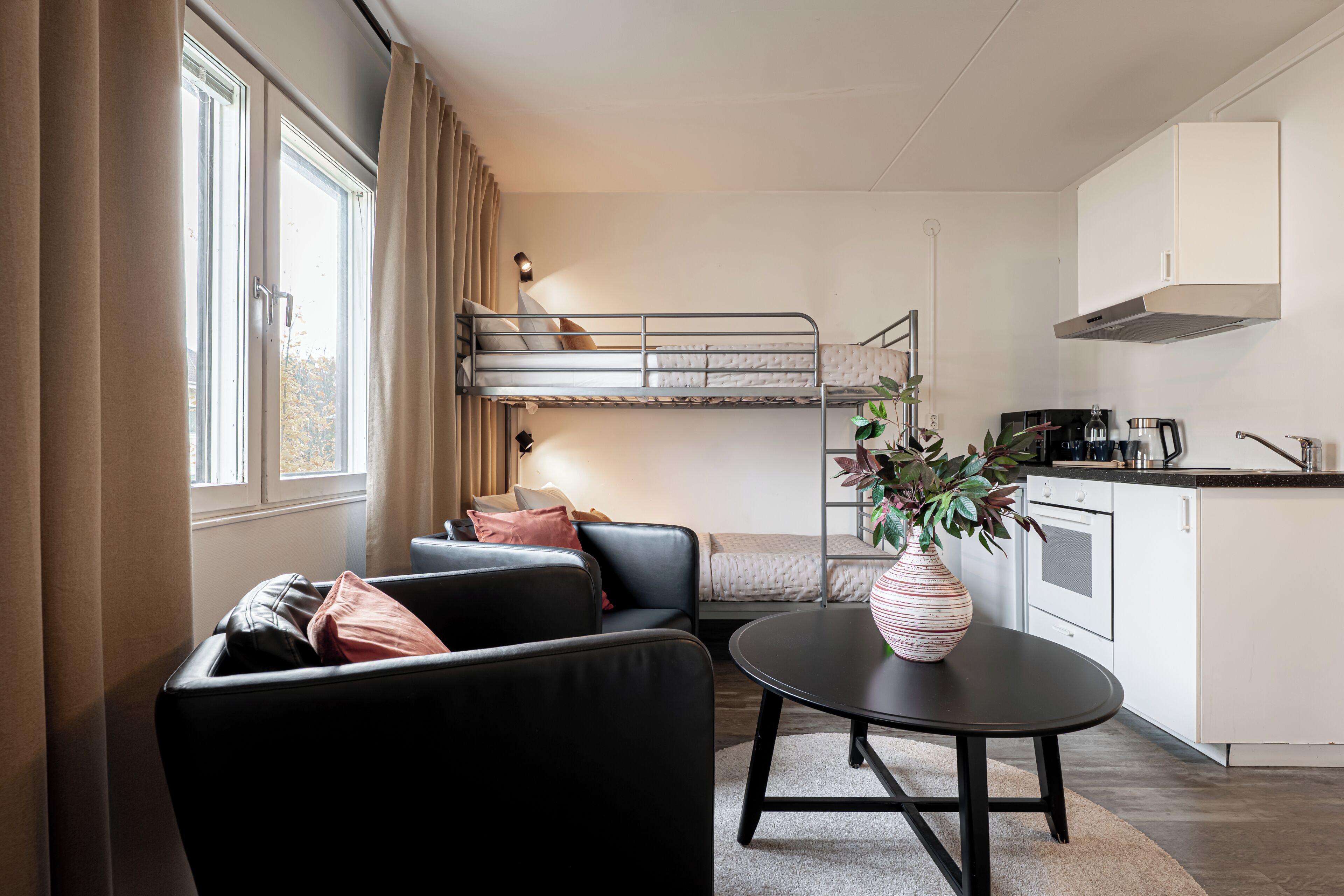 A compact living space with a bunk bed, a sofa, a dining table, and a kitchen area.