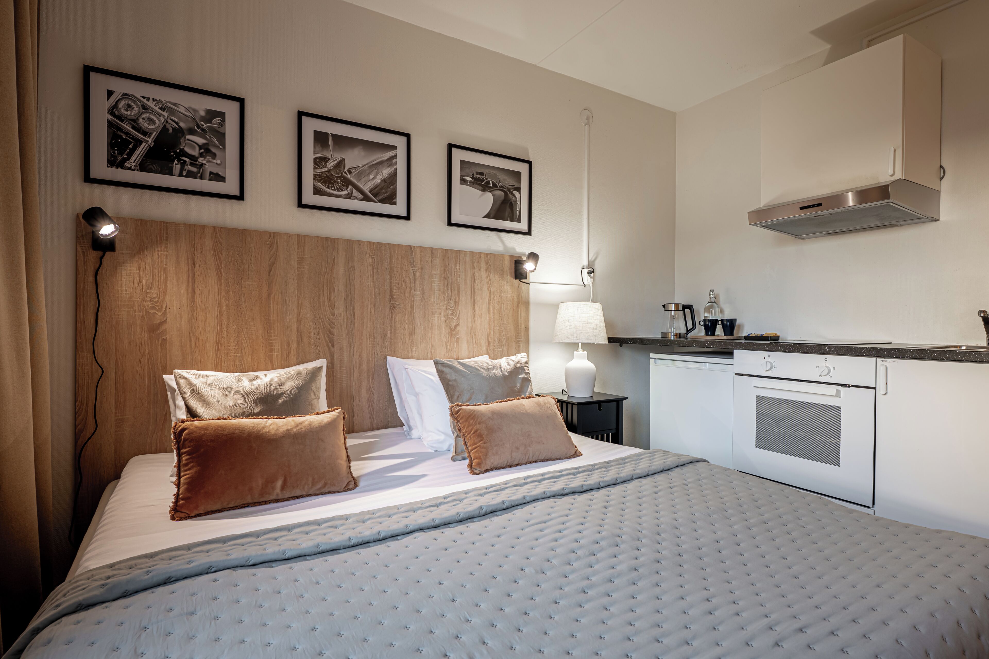 Hotellihuone, jossa on sänky, yöpöytä, lamppu, kahvinkeitin ja pieni keittiö.