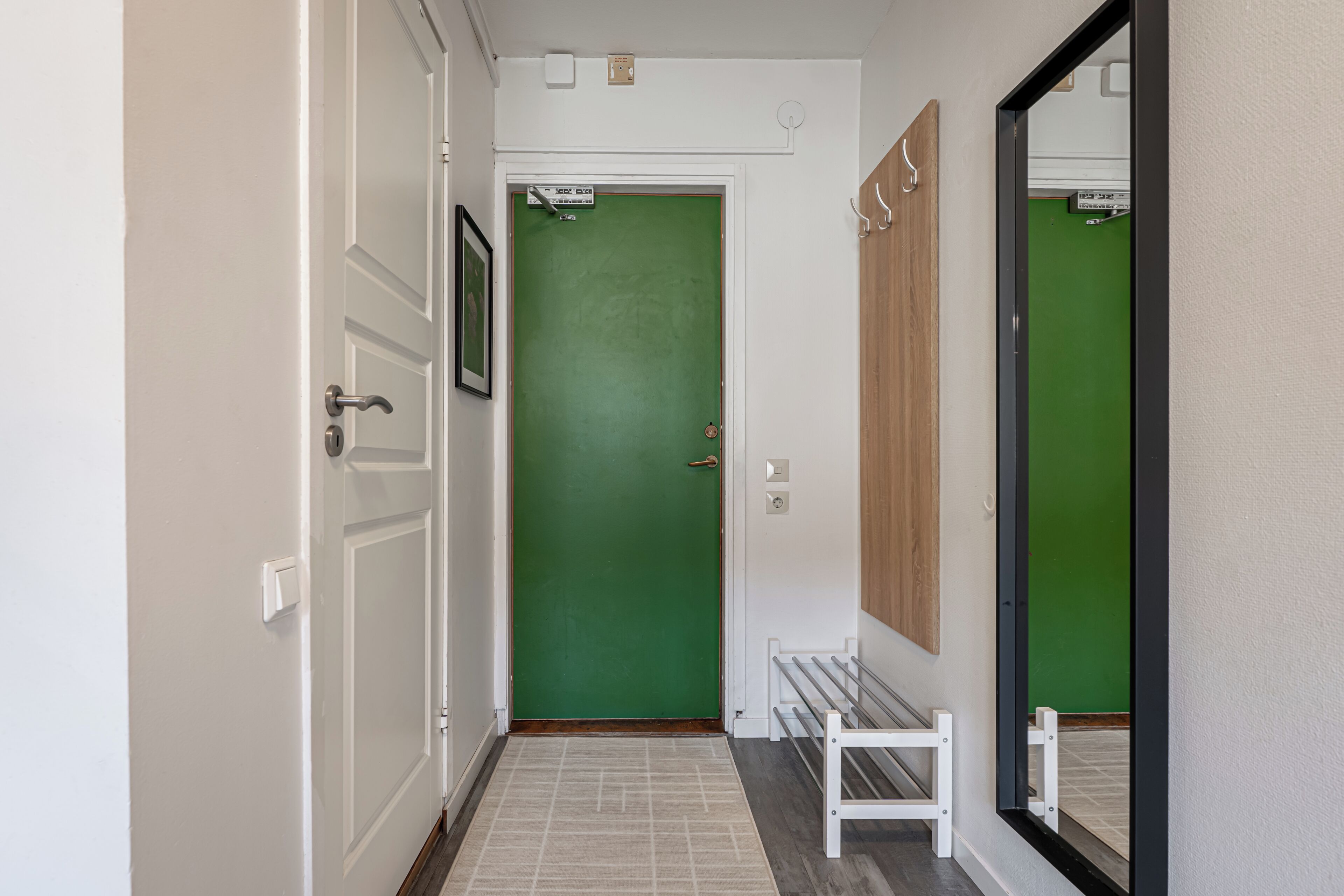 Un pasillo con una puerta verde, un banco blanco y un espejo en la pared.