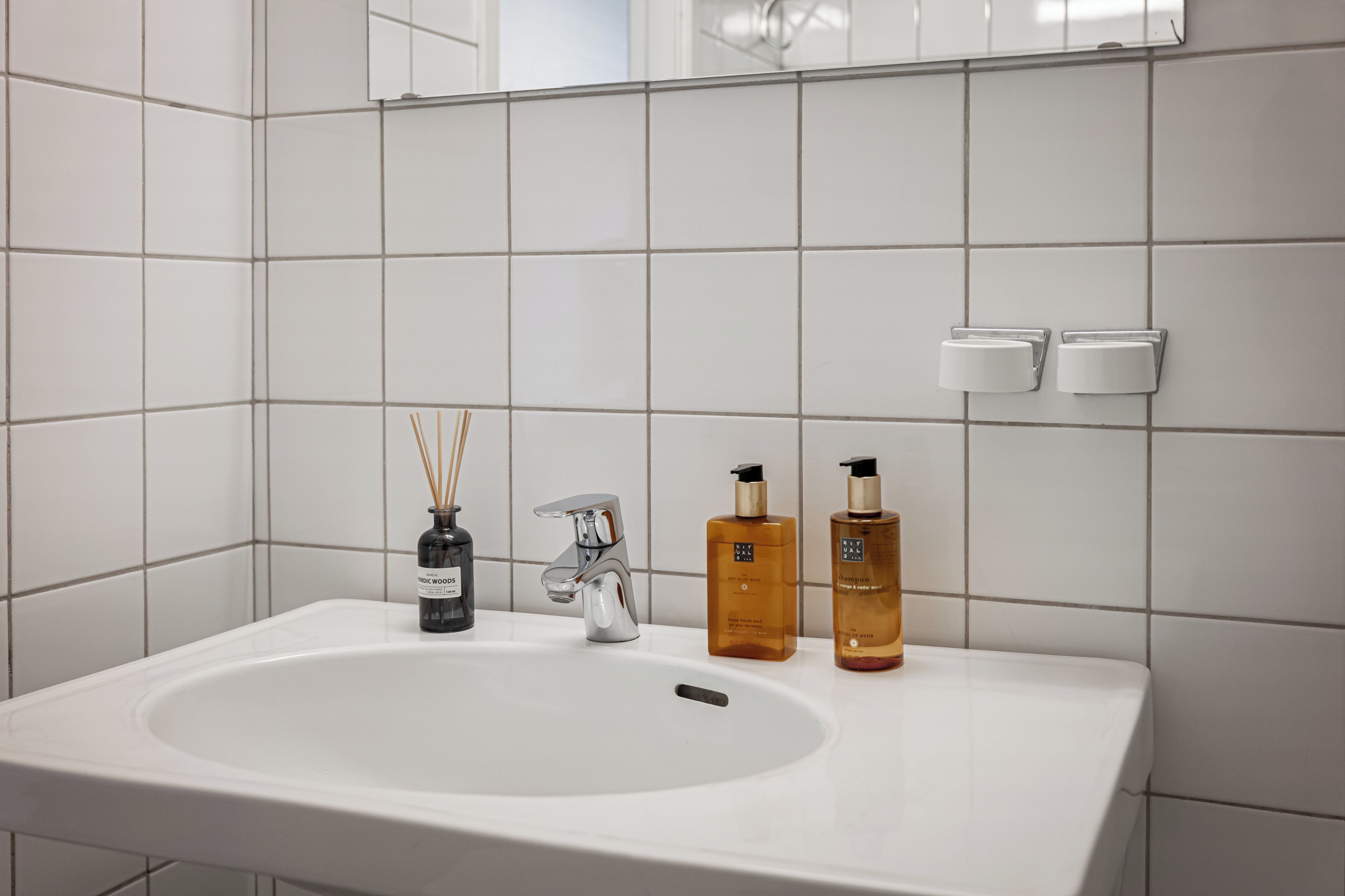 Une salle de bain avec un lavabo blanc, un miroir et deux distributeurs de savon.