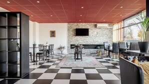 Un hall d’entrée avec un sol à carreaux, un mur en pierre orné d’un téléviseur à écran plat et un espace détente avec des chaises et des tables.