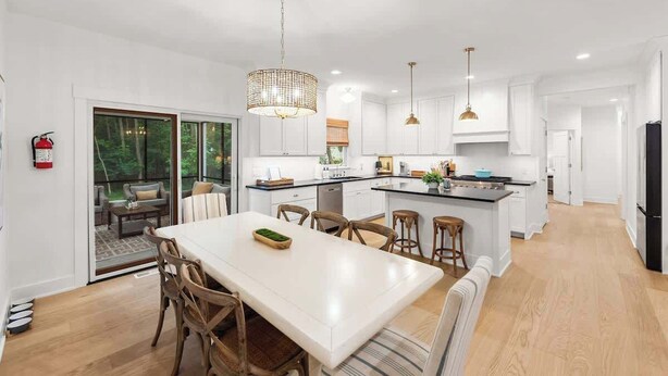 A modern kitchen with white cabinetry, a central island, pendant lighting, and a dining area with a table and chairs.
