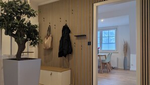 A modern interior with a wooden slat wall, a potted plant, a coat rack, and a dining area with chairs and a table. - ***SANDLOFT*** (Sankt Peter-Ording)