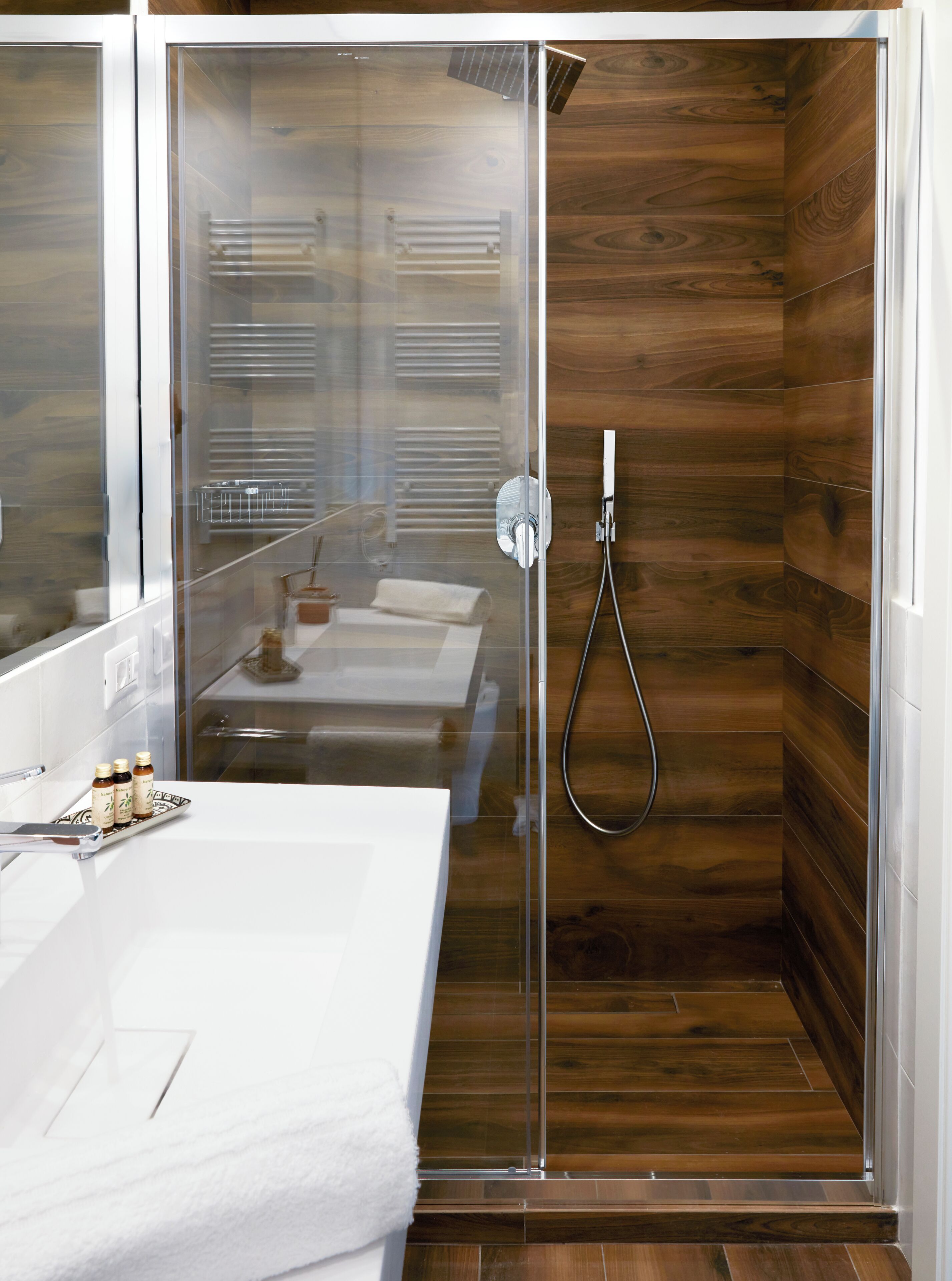 Un bagno moderno con cabina doccia in vetro, rivestimento in legno e lavabo bianco con articoli da toilette.