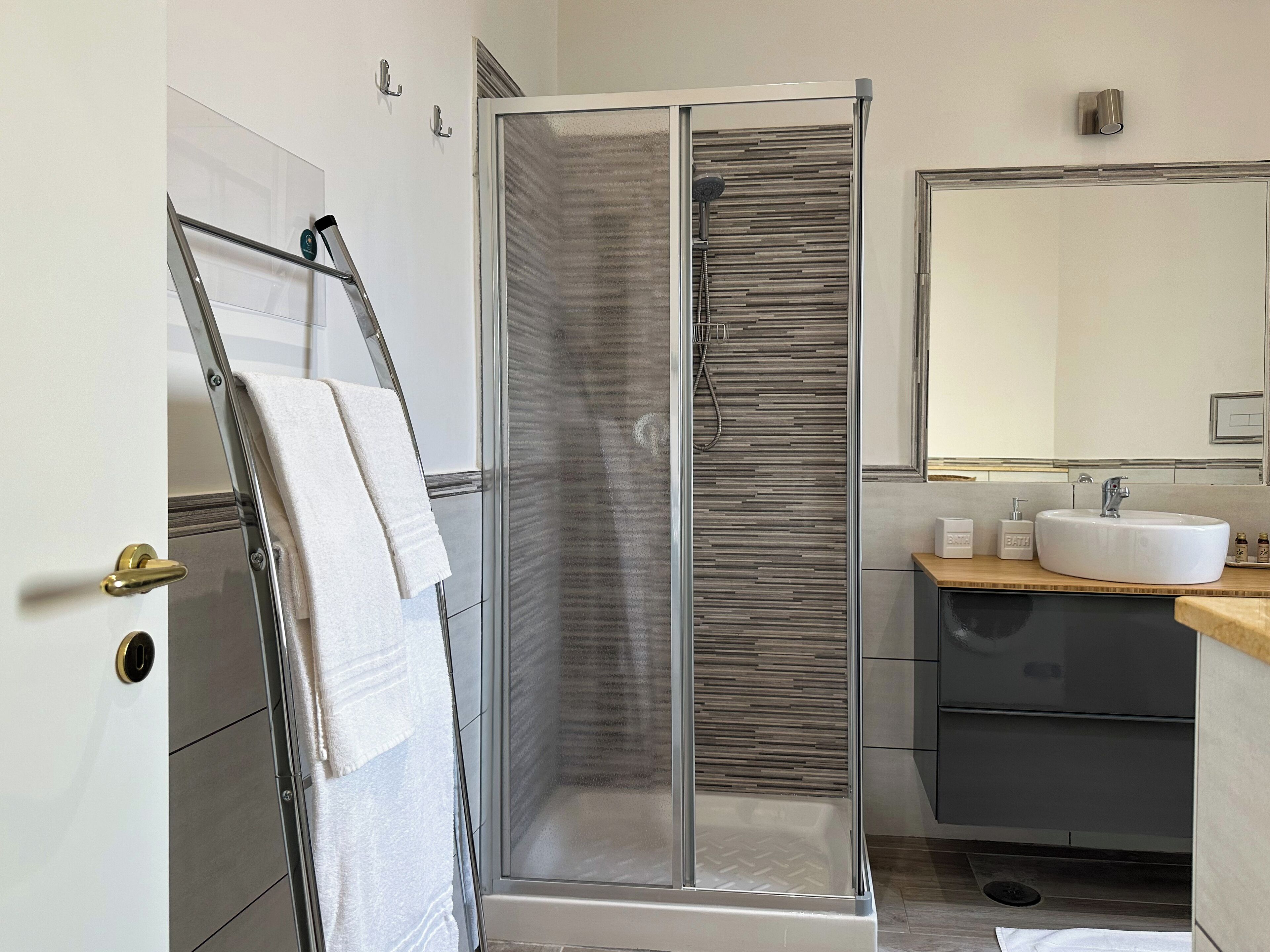 Un bagno moderno con doccia vetro, lavandino e specchio.