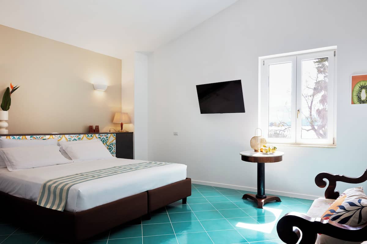 A bedroom with a bed, a bedside table, a wall-mounted TV, and a window.