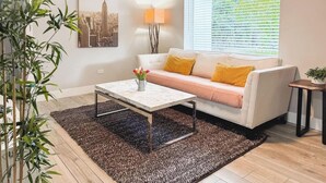 A living room with a sofa, a coffee table, a lamp, and a window with blinds. - House with Hot Tub, 10 mins to the Beach (Miami)