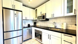 A modern kitchen with stainless steel appliances, white cabinetry, and a black countertop. - House with Hot Tub, 10 mins to the Beach (Miami)