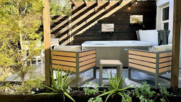 A wooden pergola with a hot tub and seating area, surrounded by greenery. - House with Hot Tub, 10 mins to the Beach (Miami)