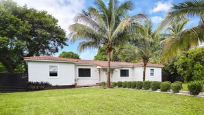 A white house with a red-tiled roof, a well-maintained lawn, and several palm trees. - House with Hot Tub, 10 mins to the Beach (Miami)