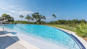 A clear blue swimming pool with a metal ladder, surrounded by greenery and a clear sky.