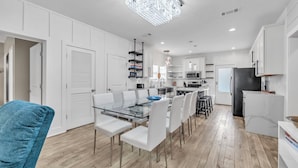 A modern kitchen with white cabinets, a glass dining table, and a chandelier.